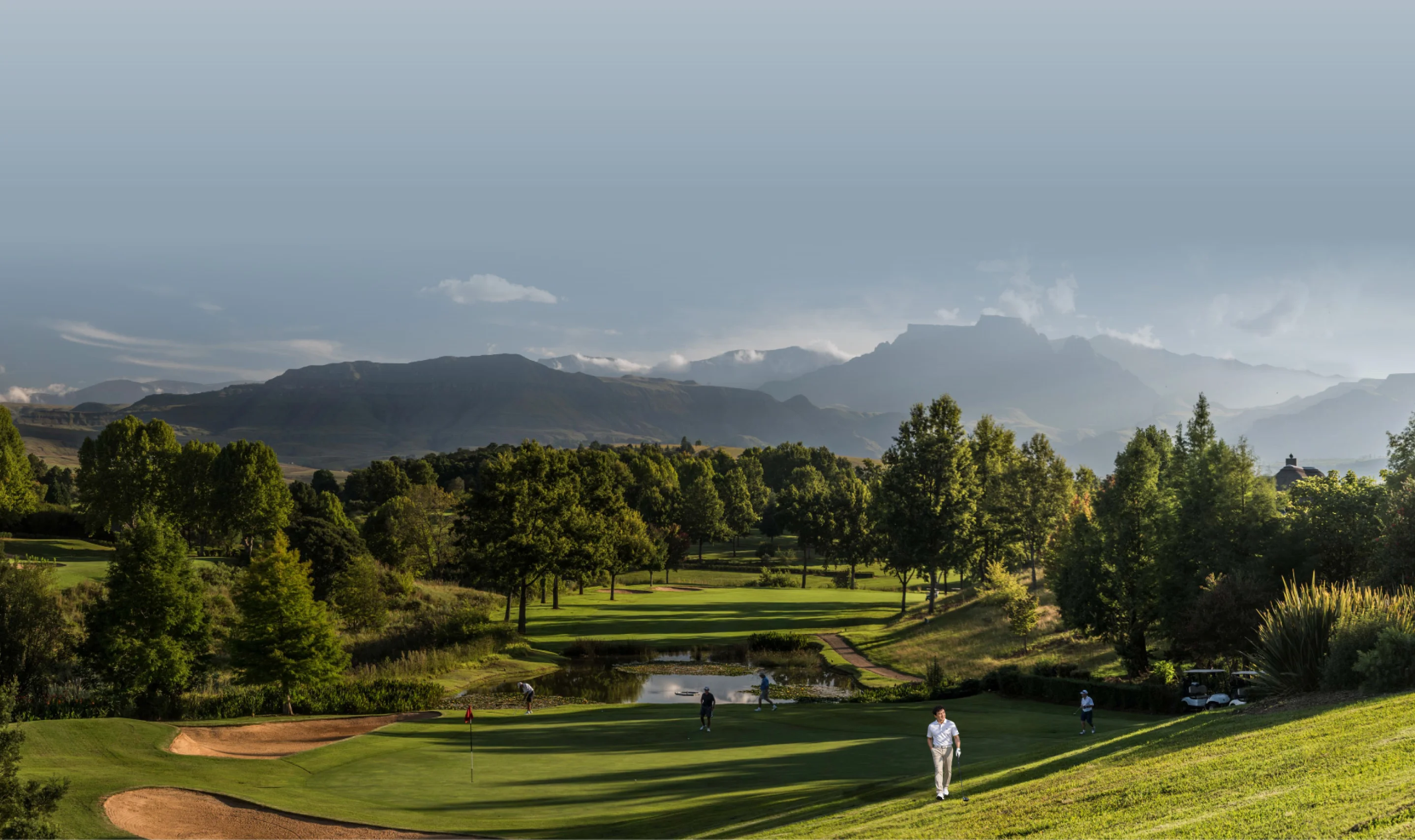 Golfers on the fairway at Champagne Sports Resort with Drakensberg peaks beyond