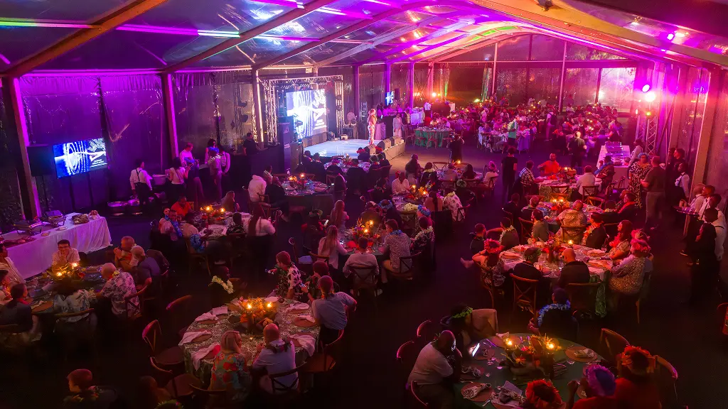 An aerial view of the SATNAC 2025 gala dinner inside a marquee, with round tables, floral centrepieces, and purple and pink lighting.