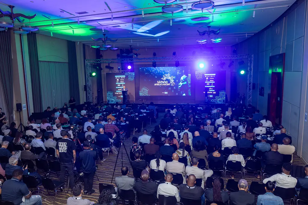 A packed plenary session at SATNAC 2025, with delegates seated before a stage displaying the Africa's Ascent theme and sponsor branding.