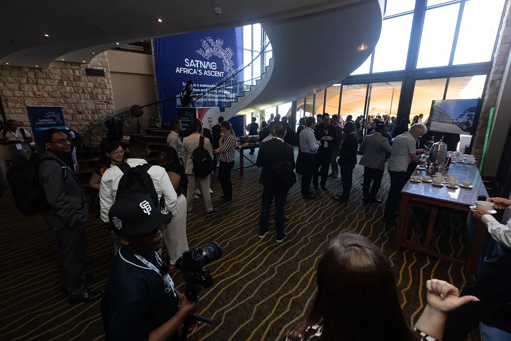 Delegates networking during a coffee break at SATNAC 2025, with Africa's Ascent branding visible in the venue foyer.